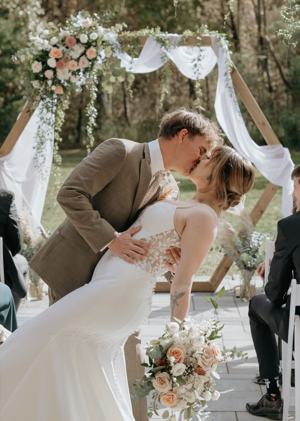 A groom dips his bride for a kiss in the aisle, her bouquet still in her hand and the draped arbour behind them
