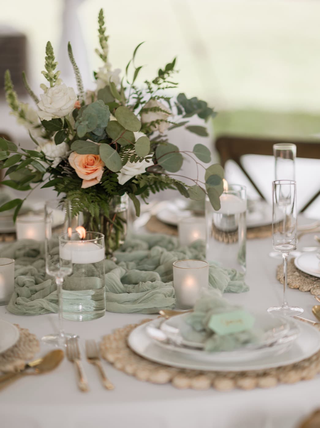 A centrepiece of white and peach roses with eucalyptus and ferns, floating candles and a sage runner around it