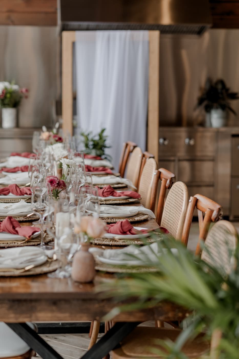 The long table set with rust and cream napkins and cane-backed chairs, the outdoor kitchen behind
