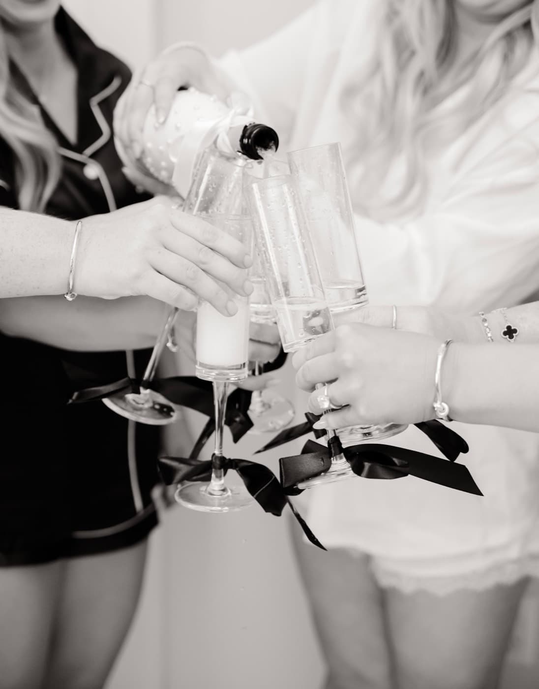 Champagne being poured into ribbon-tied flutes held by the wedding party while getting ready